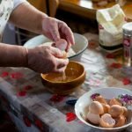 Senior woman cracking eggs into a bowl for cooking in a cozy kitchen setting.
