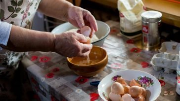 Senior woman cracking eggs into a bowl for cooking in a cozy kitchen setting.