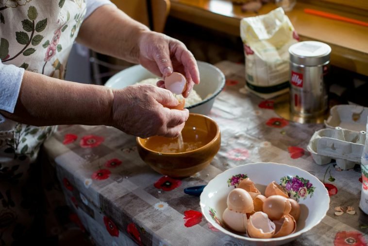 Senior woman cracking eggs into a bowl for cooking in a cozy kitchen setting.