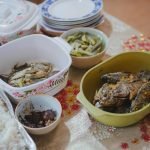Close-up of a home-cooked meal with fried fish, vegetables, and rice, displayed on a decorated table.