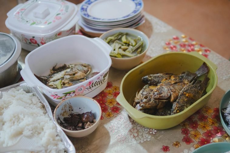 Close-up of a home-cooked meal with fried fish, vegetables, and rice, displayed on a decorated table.