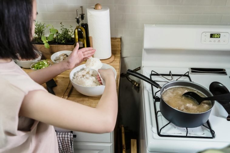 A woman in a kitchen cooking and preparing rice for a meal. Indoor setting with focus on food preparation.