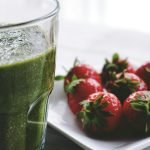 Close-up of a green smoothie and fresh strawberries on a white saucer.
