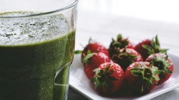 Close-up of a green smoothie and fresh strawberries on a white saucer.