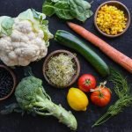 Vibrant selection of fresh vegetables including cauliflower, carrots, and broccoli arranged creatively on a dark background.