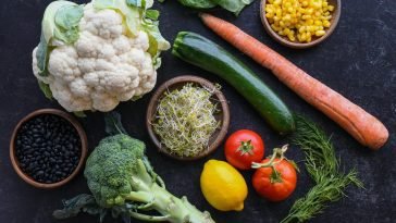 Vibrant selection of fresh vegetables including cauliflower, carrots, and broccoli arranged creatively on a dark background.