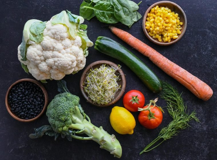 Vibrant selection of fresh vegetables including cauliflower, carrots, and broccoli arranged creatively on a dark background.