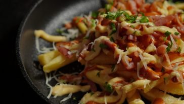 Delicious close-up of loaded French fries with melted cheese, bacon, and herbs.