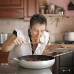 A woman savoring the aroma of a freshly cooked dish in a cozy kitchen setting.
