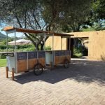 A rustic drink cart set outdoors by a river, offering beverages.