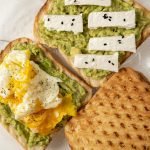 Delicious avocado toast topped with poached egg and cheese on a white plate.