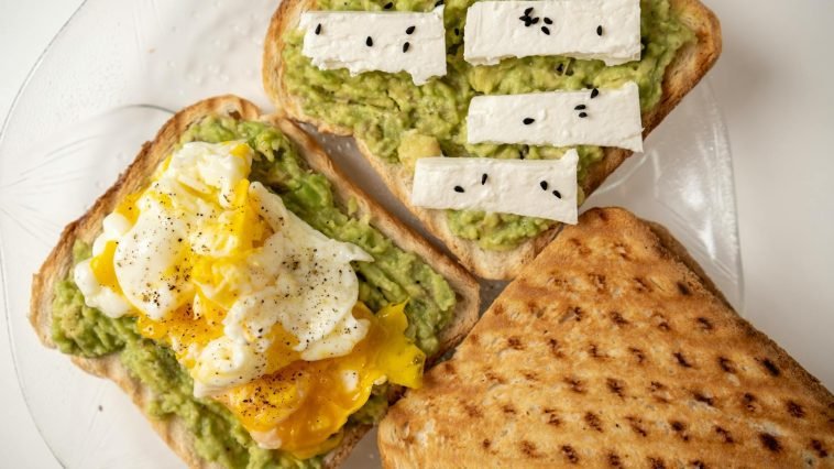 Delicious avocado toast topped with poached egg and cheese on a white plate.