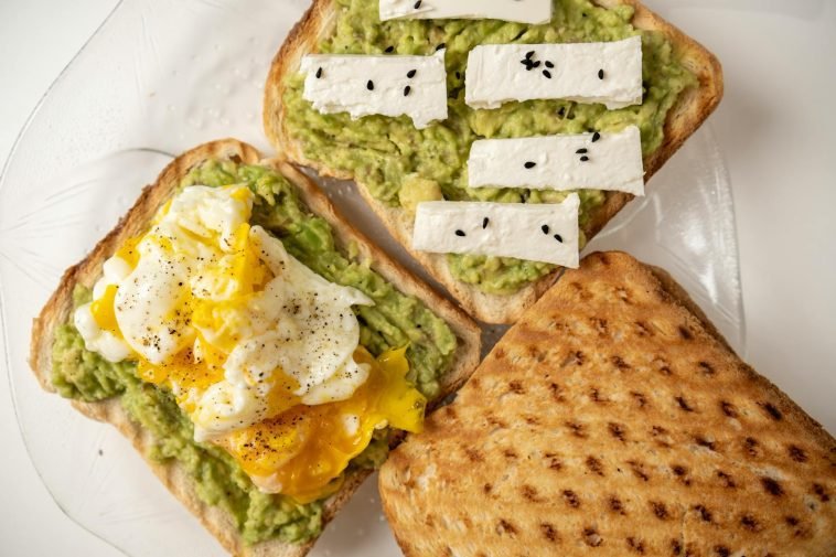 Delicious avocado toast topped with poached egg and cheese on a white plate.