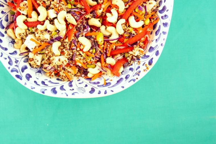 Vibrant quinoa salad with cashews, red peppers, and vegetables on a green background.