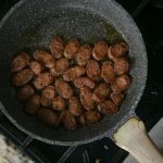 A mouth-watering view of sliced sausages cooking in a frying pan on a stove.