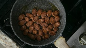 A mouth-watering view of sliced sausages cooking in a frying pan on a stove.