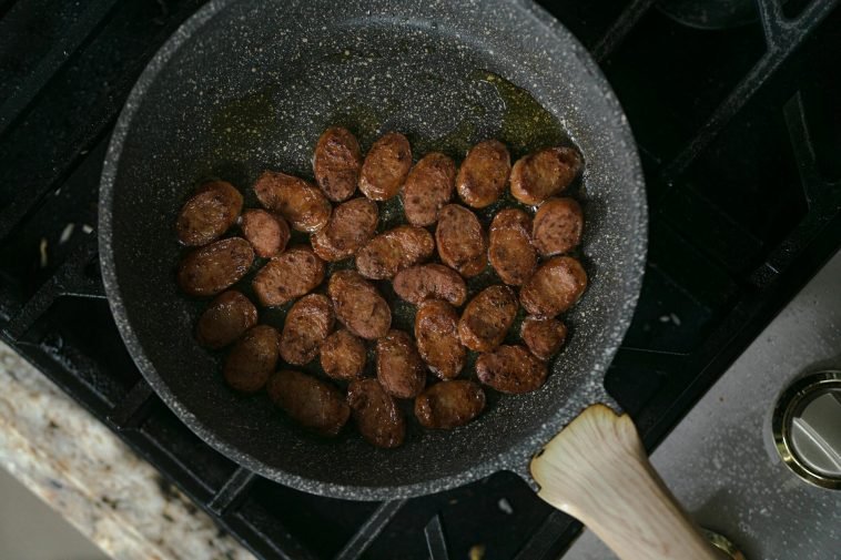 A mouth-watering view of sliced sausages cooking in a frying pan on a stove.
