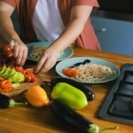 Woman arranging fresh vegetables and pasta on plates in a kitchen setting.