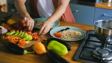 Woman arranging fresh vegetables and pasta on plates in a kitchen setting.