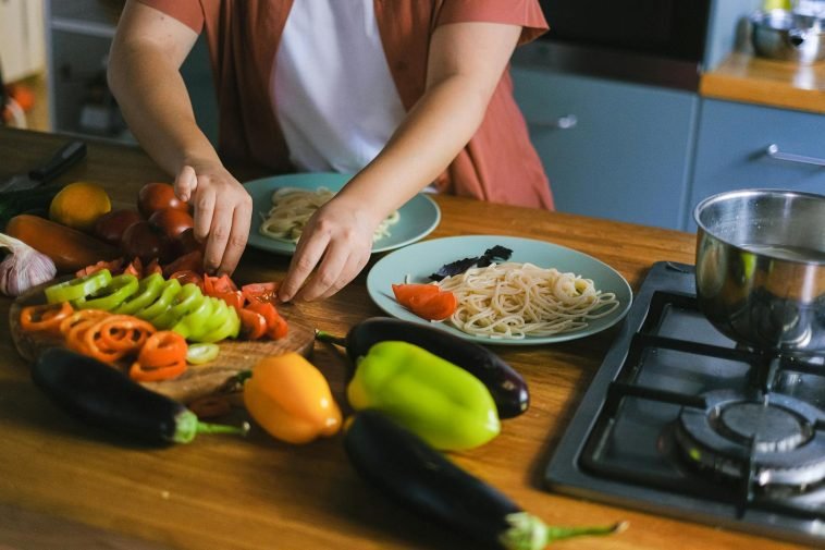 Woman arranging fresh vegetables and pasta on plates in a kitchen setting.