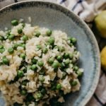 Tasty risotto with green peas on a ceramic plate, accompanied by fresh lemons.