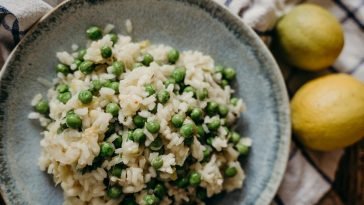 Tasty risotto with green peas on a ceramic plate, accompanied by fresh lemons.