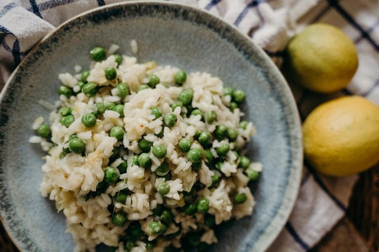 Tasty risotto with green peas on a ceramic plate, accompanied by fresh lemons.