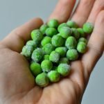 Close-up of a hand holding frozen green peas, showcasing freshness and texture.