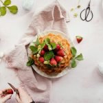 Homemade cake with strawberries on a pink cloth, surrounded by Easter eggs.