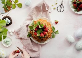 Homemade cake with strawberries on a pink cloth, surrounded by Easter eggs.