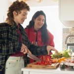 Two young women happily preparing a healthy meal with fresh vegetables in a bright kitchen setting.