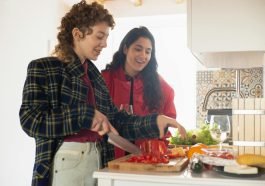 Two young women happily preparing a healthy meal with fresh vegetables in a bright kitchen setting.