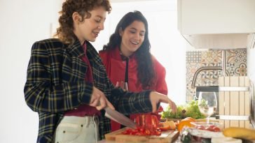 Two young women happily preparing a healthy meal with fresh vegetables in a bright kitchen setting.