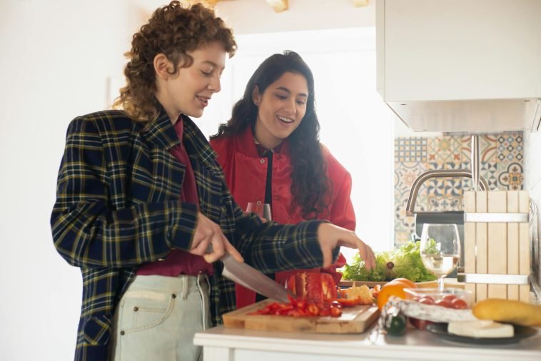 Two young women happily preparing a healthy meal with fresh vegetables in a bright kitchen setting.