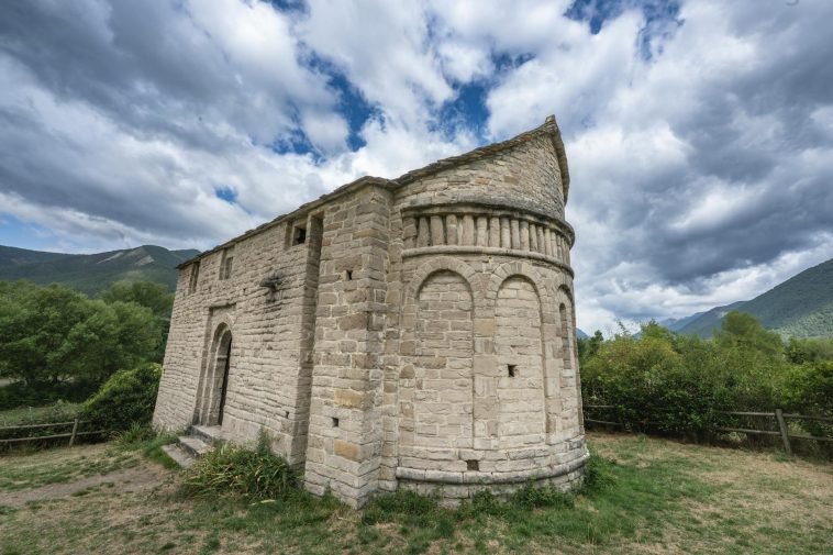 Historic Romanesque church in Huesca, Aragón, with a dramatic cloudy sky background.
