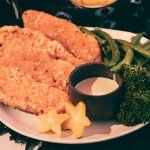 Crispy fried chicken fillets with broccoli, green beans, and star fruit on a plate.