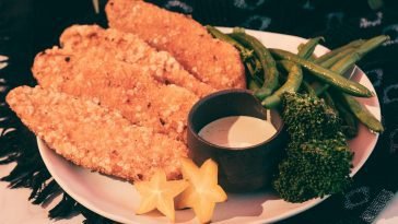 Crispy fried chicken fillets with broccoli, green beans, and star fruit on a plate.