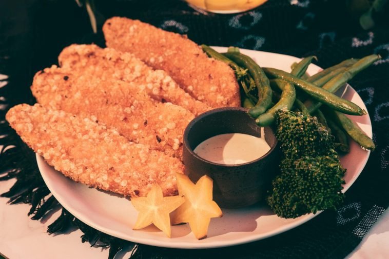 Crispy fried chicken fillets with broccoli, green beans, and star fruit on a plate.