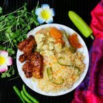 A vibrant dish featuring fried rice with vegetables, glazed chicken, and fresh herbs, garnished with flowers.