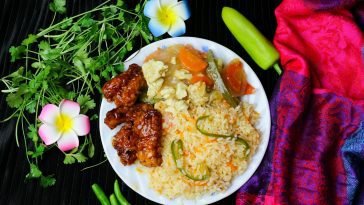 A vibrant dish featuring fried rice with vegetables, glazed chicken, and fresh herbs, garnished with flowers.