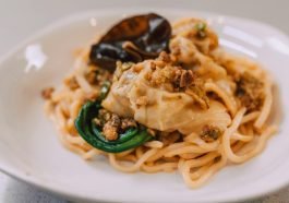 A delicious Asian noodle dish topped with dumplings and garnished on a plate.