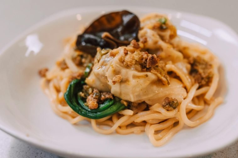 A delicious Asian noodle dish topped with dumplings and garnished on a plate.