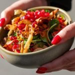 Close-up of a vibrant vegetable salad with pomegranate seeds and crispy toppings in a bowl.
