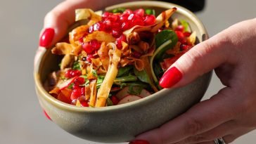 Close-up of a vibrant vegetable salad with pomegranate seeds and crispy toppings in a bowl.