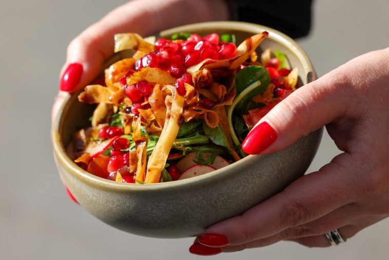 Close-up of a vibrant vegetable salad with pomegranate seeds and crispy toppings in a bowl.