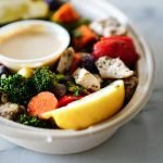A nutritious bowl of vegetables and chicken served with dipping sauce and lemon slices.
