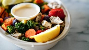 A nutritious bowl of vegetables and chicken served with dipping sauce and lemon slices.