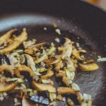 Close-up of sliced mushrooms and onions sautéing in a skillet, showcasing cooking detail.