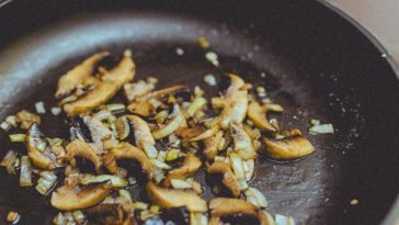 Close-up of sliced mushrooms and onions sautéing in a skillet, showcasing cooking detail.