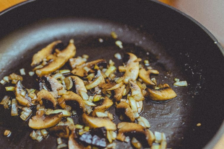 Close-up of sliced mushrooms and onions sautéing in a skillet, showcasing cooking detail.